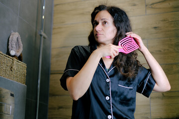Woman in pajamas combing her curly hair in bathroom