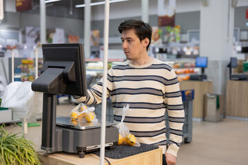 A young man weighs goods on scales in a supermarket. A male shopper in a self-service store.