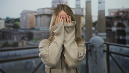 Woman with blonde hair waves both hands with open palms on street in rome near ancient ruins; playfulness joy.