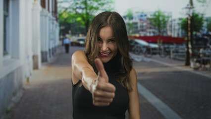 Young hispanic woman showing dual thumbs up gesture on vibrant urban street with blurred building facades; optimism.