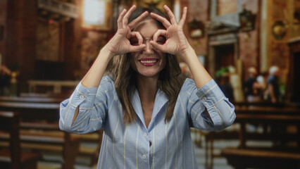 Woman smiling and looking through her hands as binoculars in ancient building; curiosity playfulness.