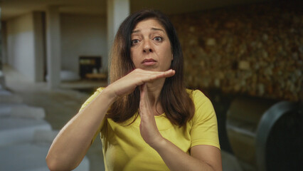 Woman makes timeout sign with hands at indoor spa pool lounge surrounded by tiled walls; calm pause.