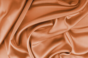 Crumpled, wrinkled orange colored glossy silk satin with wave drapery. Shiny smooth fabric with soft folds, cloth texture . Elegant rich background, wallpaper, backdrop. Flat lay, top view