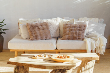 Comfortable white sofa with decorative pillows, cushions and wooden coffee table in cozy minimalist...