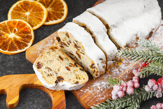 Traditional Christmas stollen, sweet fruit loaf sliced on wooden board, dusted with powdered sugar on black textured background. Spices, dried fruits and festive decorations create winter holiday mood - Powered by Adobe