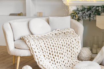 Neutral white boucle sofa with chunky knitted blanket with soft pillows in a cozy festive living room. Design of bright minimal scandinavian interior decorated round and square cushion on couch