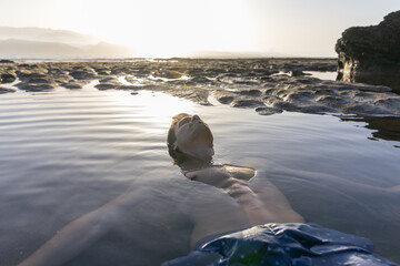 Close-up of a boy floating on the shore of a pebble beach at sunset