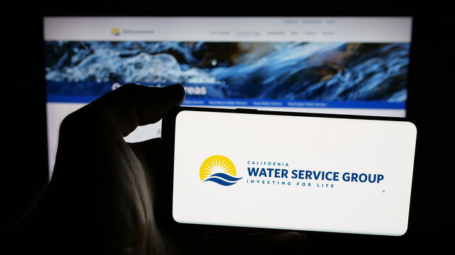 Stuttgart, Germany - 11-27-2025: Person holding mobile phone with logo of US company California Water Service Group on screen in front of web page. Focus on phone display.