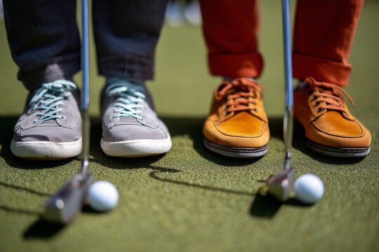 Two people standing on a green field with golf shoes and a golf ball