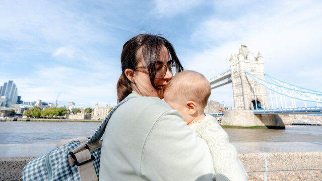 Mother holding baby by London Tower Bridge on sunny day