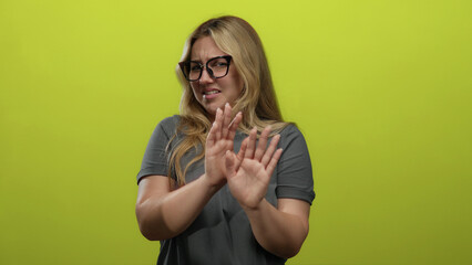 Woman expressing disgust with hands raised in front of isolated green background wearing glasses showing clear disapproval and negative emotion