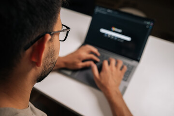 Close-up view from shoulder of office worker male wearing eyeglasses and typing on laptop keyboard,...