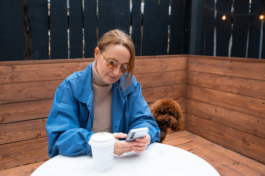 Woman with cellphone and dog at outdoor cafe table