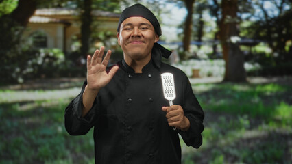 Man chef in black uniform waving hand and holding metal grater in forest  warm hospitality contentment. © Krakenimages.com