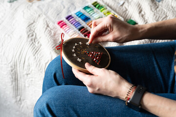 A person sits on a chair stitching a christmas tree on dark fabric using a needle and thread....