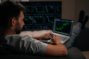 View from shoulder of trader analyzing cryptocurrency and stock market charts, monitoring investment data on multiple screens, managing finance portfolio at home, working on laptop in dark room.