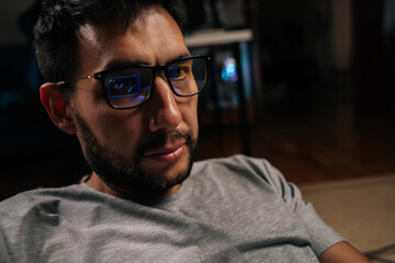 Male trader wearing blue light filtering glasses, intently watching computer screen with financial charts reflecting in lenses, trading stocks and cryptocurrency at night. Concept of online trading.