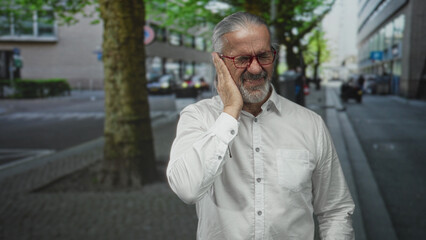 Man pressing hands to ears on a busy street near a tree and storefronts; distress noise sensitivity.