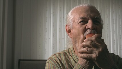 The man is seen biting into a bright red apple in his hand with great pleasure and appetite, and the sincere happiness and pleasure on his face are clearly visible.