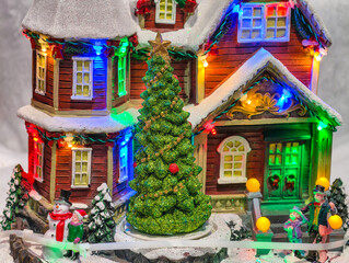 Fototapeta premium Christmas Village Miniature House with Colorful LED Lights, Glitter Tree and Snowman Figurines for Holiday Decoration Background 