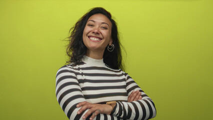 Fototapeta premium Woman face smiling with teeth, head tilted, wearing hoop earrings and black white striped sweater in bright lime green studio; joy confidence.