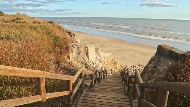 Wooden boardwalk steps descend a sandy cliff to the vast Atlantic beach at Cuesta Maneli, Huelva, Spain. Nature, travel destination, scenic view.