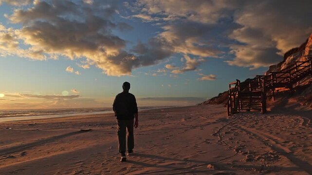 Silhouette of a man walking alone on the sand at Cuesta Maneli beach, Huelva, Spain, during a peaceful sunset. Travel, freedom, and solitude concept.