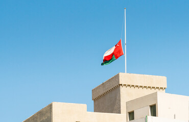 Omani flag displayed on the exterior of a building, standing out against a clear blue sky.