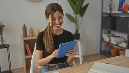 Woman taps blue tablet with fingers while seated at a wooden desk in home studio; serene...