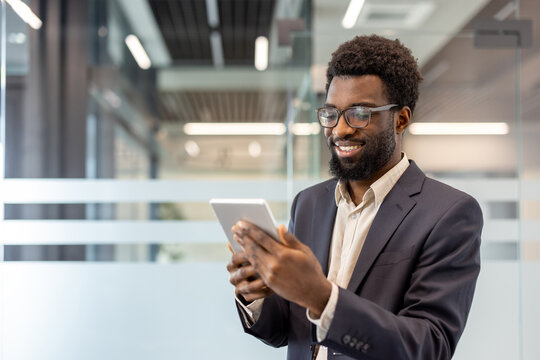 African american businessman smiling, browsing content on a digital tablet, representing technology integration, success, and connectivity in a contemporary corporate environment