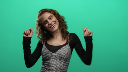 Woman dancing happily with a joyful smile against a vibrant green background isolated from other elements in the scene, highlighting her youthful energy and carefree spirit.