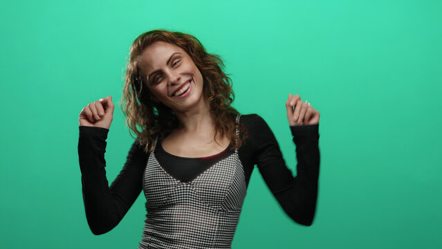 Woman dancing happily with a joyful smile against a vibrant green background isolated from other elements in the scene, highlighting her youthful energy and carefree spirit. - Powered by Adobe