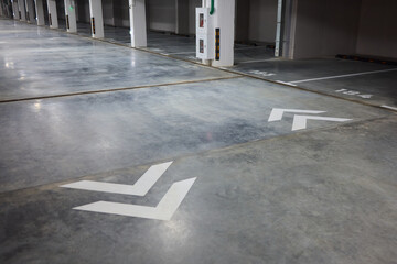 Brightly marked vehicle storage area, Concrete structure with guiding arrows and lighting, Industrial style subterranean garage with safety features and signage present