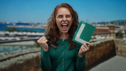 Woman celebrating success by the seaside holding keys and a learner's permit; joyful expression highlights her achievement at the scenic coastal port setting.