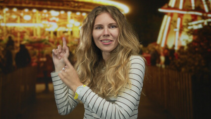 Woman holds her hands presenting a carnival full of lights as a blonde young host smiling with amusement at the night attraction.