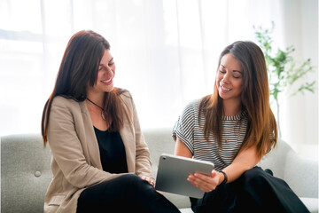 Two female colleagues enjoying break in the office sit on sofa