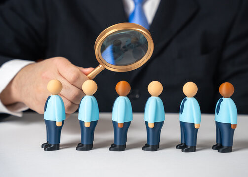 A businessman examines a line of job applicants through a magnifying glass. Careful hiring, talent search and strict selection criteria. Recruitment, labor market and candidate evaluation.