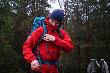 A young man puts a hiking backpack on his shoulders and fastens the straps with fasteners.