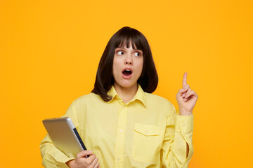A surprised young woman in a yellow shirt holds a tablet, pointing up as she reacts to a surprising idea. The bold orange backdrop adds energy and focus to the scene.