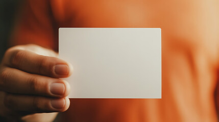 Hand holding a blank card with a blurred orange background.  The white card is held by a person and is ready to display a message or information. Simple and clean