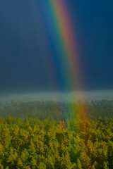 A vivid rainbow brightens the stormy sky above a green town landscape with a church tower in the foreground