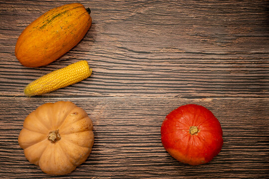 Autumn flat lay with pumpkins, squash and corn arranged on the left side of dark wood with large copy space