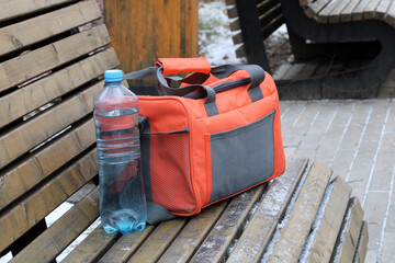 refrigerator bag and water bottle on park bench in winter