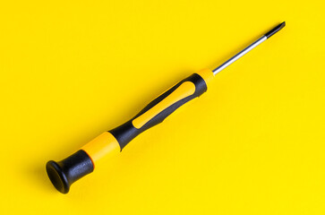 Close-up of a yellow and black screwdriver on a bright yellow background
