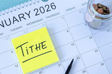 Tithe handwritten text on sticky note on top of January 2026 calendar year and coins. Top view. Christian finances, giving, and offering, biblical concept.