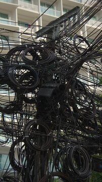 cables wrapped around pole, electrical cords entangle around modern building in bustling cityscape