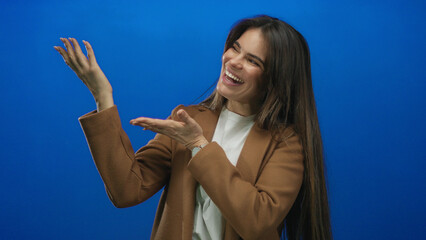 Smiling hispanic young woman gestures playfully against an isolated blue background in a stylish...