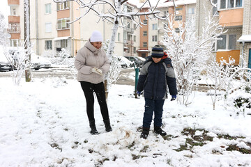 A woman and a boy are playing with snowballs, trying to make a snowman.