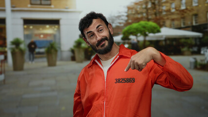 Hispanic man with a beard and orange jumpsuit stands outdoors on a street, showcasing playful gestures and expressing friendliness.