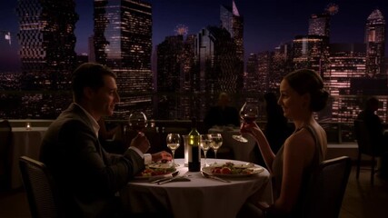 A couple enjoying a romantic dinner on a rooftop restaurant overlooking a city skyline at night Stock Video